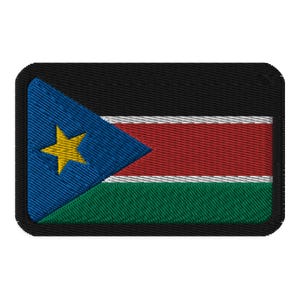 May include: A black embroidered patch featuring the flag of South Sudan. The flag design includes a blue triangle with a yellow five-pointed star in the top left corner, a red horizontal stripe, a white horizontal stripe, and a green horizontal stripe.