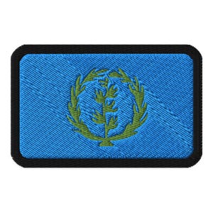 Könnte beinhalten: Gestickter Aufnäher mit der Flagge Eritreas. Der Aufnäher hat einen hellblauen, strukturierten Hintergrund. Ein grüner Kranz umgibt einen grünen Olivenzweig. Der rechteckige Aufnäher hat abgerundete Ecken und einen schwarzen Rand.