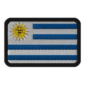 Pode incluir: Um remendo bordado preto com a bandeira do Uruguai. A bandeira apresenta um desenho de listras azuis e brancas com um sol amarelo no canto superior esquerdo.