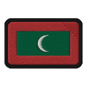 May include: Embroidered patch featuring the flag of the Maldives. The design includes a green rectangle with a white crescent moon, framed by a red border and a black outer edge. The patch has a textured, stitched appearance.