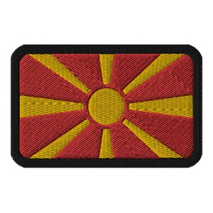 May include: A red and yellow embroidered patch featuring the flag of North Macedonia. The flag has a yellow sun with eight rays on a red background.