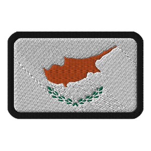 May include: A white embroidered patch with a black border featuring the flag of Cyprus. The flag depicts a copper-colored outline of the island of Cyprus with a green olive branch wreath below.