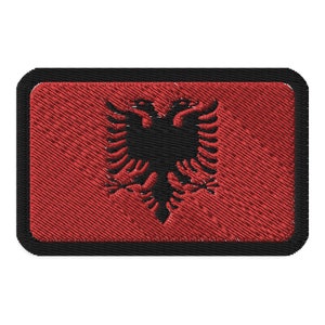 May include: A red embroidered patch with a black double-headed eagle, the national symbol of Albania, centered on the patch. The patch has a black border.