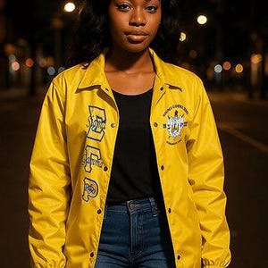 May include: A yellow jacket with blue lettering and a crest on the chest. The jacket is worn over a black shirt and blue jeans. The jacket has the words "Sigma Gamma Rho" on the front.