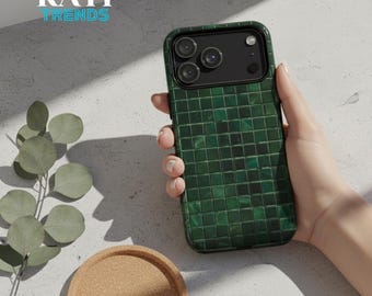 May include: Green phone case with a square tile pattern, held by a hand. The case has a camera cutout and the text "KATI TRENDS" in white and teal. A cork coaster and eucalyptus sprig are in the background.
