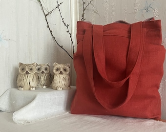 May include: A red linen tote bag with two handles. The bag is sitting on a white linen surface with three ceramic owl figurines in front of it.