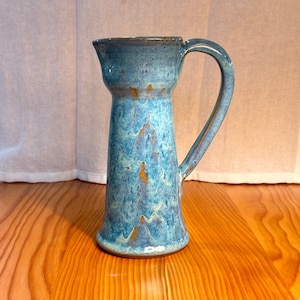 Könnte beinhalten: Ein blauer und goldener Keramik Krug mit Henkel. Der Krug hat eine strukturierte, marmorierte Glasur.