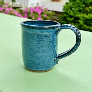 May include: A blue ceramic mug with a textured handle. The mug has a speckled glaze and a light brown rim.
