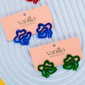 Könnte beinhalten: Ein Paar Ohrringe in abstrakter Form. Die Ohrringe sind aus Acryl und in Blau und Grün erhältlich.