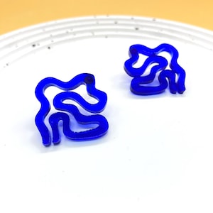 Op de afbeelding: Een paar blauwe oorringen in een abstracte vorm. De oorringen zijn gemaakt van een glad, glanzend materiaal en hebben een uniek, modern ontwerp.
