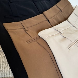 May include: Three pairs of pants in black, brown, and beige. The pants are folded and stacked on top of each other.