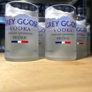 Pu&ograve; includere: Tre bottiglie di vetro trasparente di vodka Grey Goose, ciascuna con un design smerigliato e il nome del marchio stampato in blu. Le bottiglie sono da 700 ml e al 40% di alcol in volume. Le bottiglie sono appoggiate su una superficie di legno.