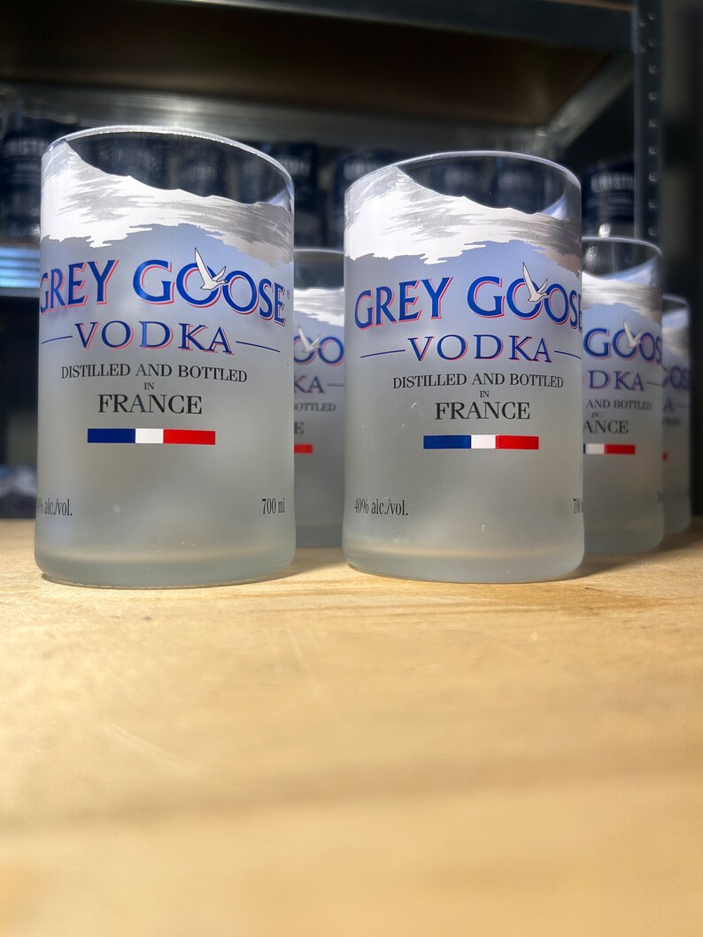 Pu&ograve; includere: Tre bottiglie di vetro trasparente di vodka Grey Goose, ciascuna con un design smerigliato e il nome del marchio stampato in blu. Le bottiglie sono da 700 ml e al 40% di alcol in volume. Le bottiglie sono appoggiate su una superficie di legno.
