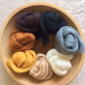 May include: A wooden bowl filled with eight different colors of wool roving. The colors are brown, orange, yellow, beige, white, gray, and black.