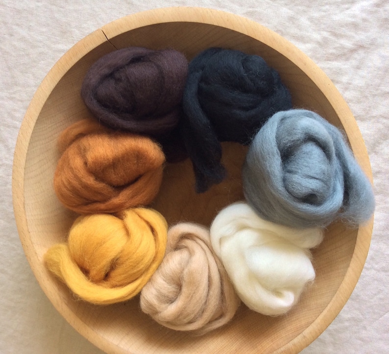 May include: A wooden bowl filled with eight different colors of wool roving. The colors are brown, orange, yellow, beige, white, gray, and black.