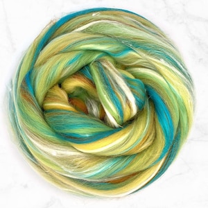 May include: A close-up of a ball of colorful fiber, featuring shades of green, yellow, blue, and white. The fiber is arranged in a swirling pattern, creating a visually appealing and textured effect.