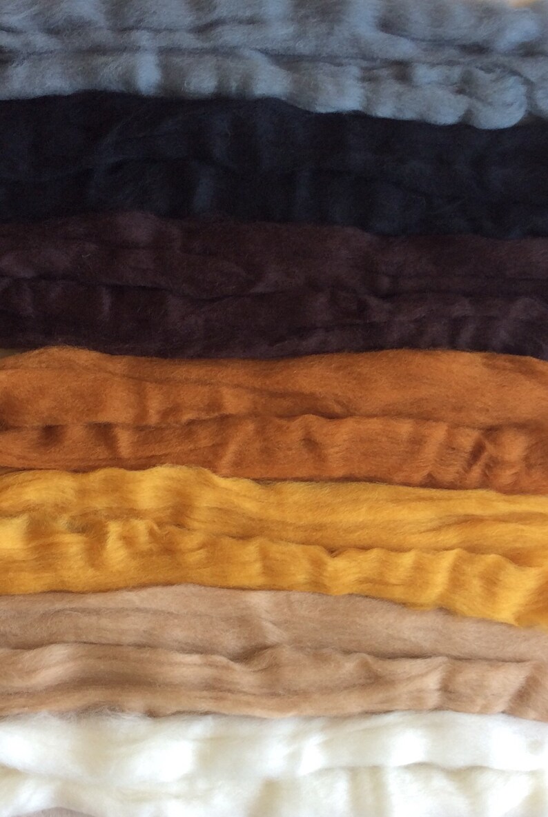 May include: A stack of different colored wool roving, including white, beige, yellow, orange, brown, black, and gray.
