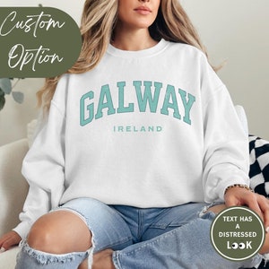 Woman wears white sweatshirt with Galway, Ireland in a marine vintage style text. Option to customise.