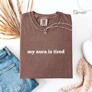 Flat lay Comfort Colors T Shirt in espresso with ‘my aura is tired’ written in bold white lower case text