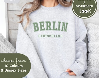 May include: A gray sweatshirt with the text "BERLIN DEUTSCHLAND" in green. The text has a distressed look. The sweatshirt is available in 10 colors and 8 sizes.