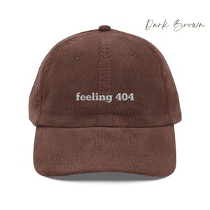 May include: A dark brown corduroy baseball cap with the text "feeling 404" embroidered in white on the front.