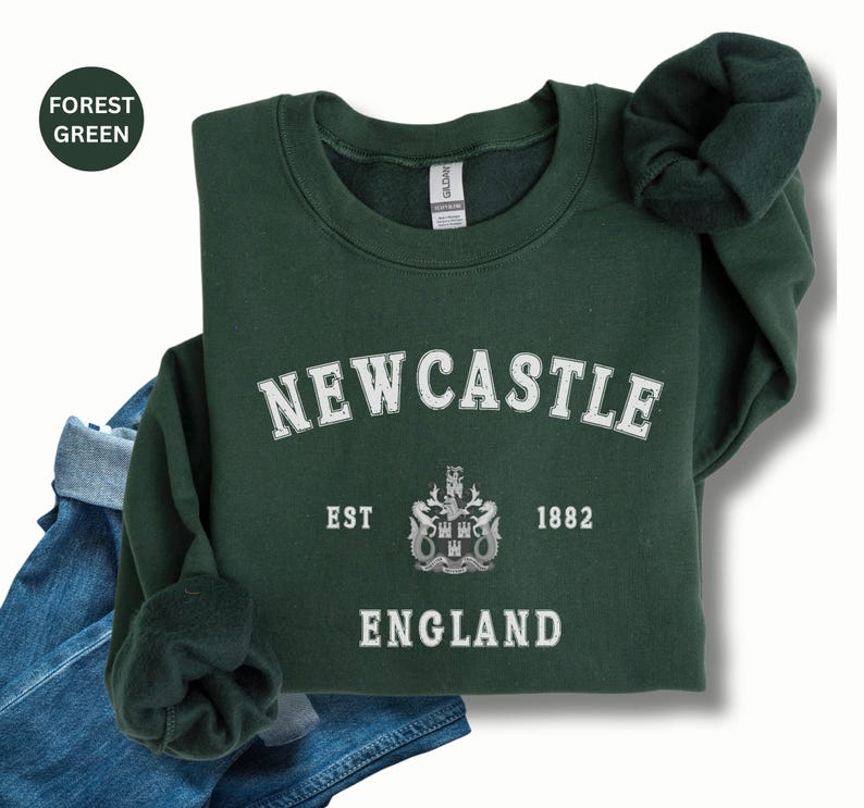 Lay flat forest green sweatshirt with Newcastle  England, EST 1882 and the Newcastle coat of arms in White distressed text. Also in royal, Black, Dark Heather, Forest Green, Navy, Sand, Sport Grey and White. Sizes from Small to XXL.