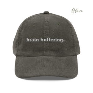 May include: Olive green corduroy baseball cap with white embroidered text that reads "brain buffering..."