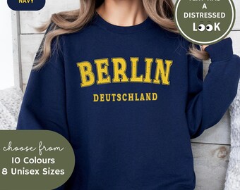 May include: A navy blue sweatshirt with the text "BERLIN DEUTSCHLAND" in yellow. The text has a distressed look.