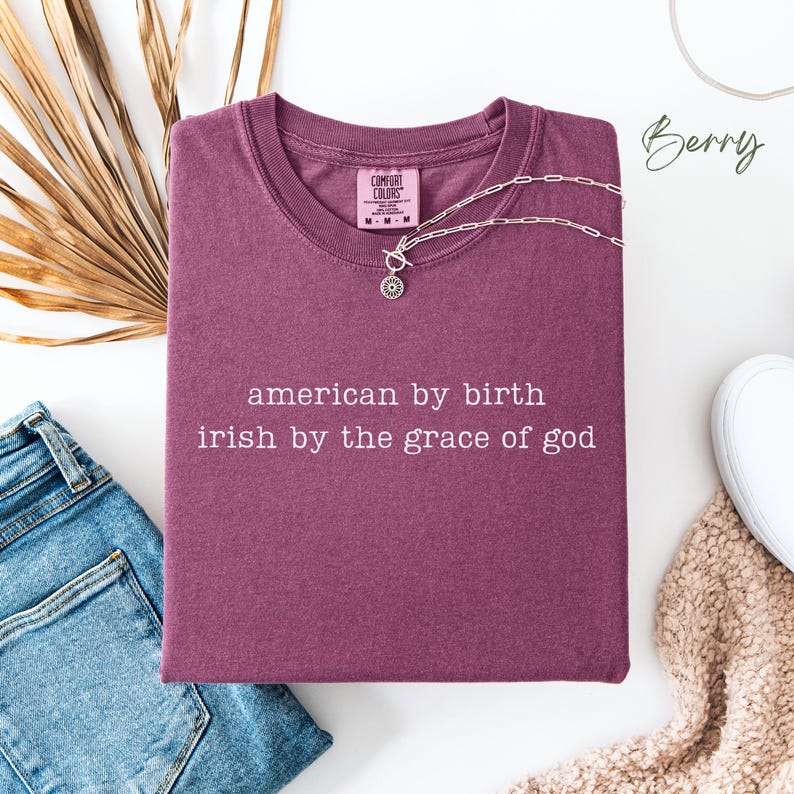 May include: A maroon t-shirt with the text "american by birth irish by the grace of god" printed in white. The shirt is made by Comfort Colors.