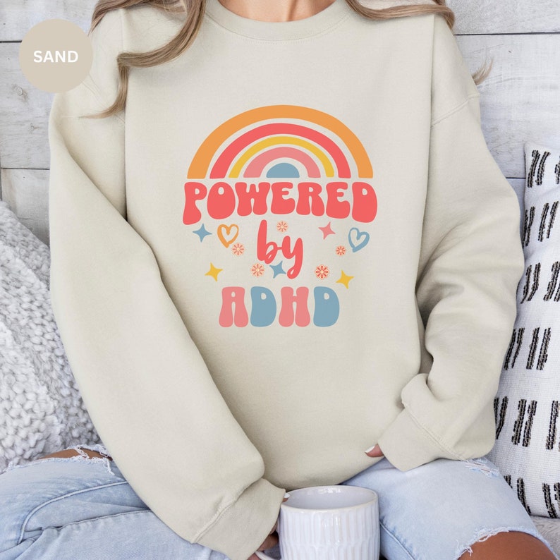 Woman wears Sand sweatshirt with slogan Powered By ADHD