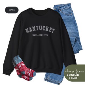 Könnte beinhalten: Schwarzer Pullover mit einem grauen Aufdruck, der "NANTUCKET MASSACHUSETTS" lautet. Der Pullover ist mit einer blauen Jeans und einem Paar rot-grauen Socken abgebildet.