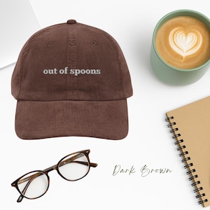 May include: A dark brown corduroy baseball cap with the text "out of spoons" embroidered in white on the front.
