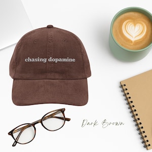 May include: A dark brown corduroy baseball cap with the text "chasing dopamine" embroidered in white on the front.