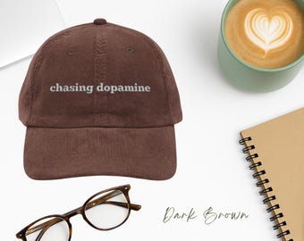 May include: A dark brown corduroy baseball cap with the text "chasing dopamine" embroidered in white on the front.