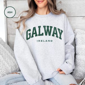 Woman wears ash grey sweatshirt with Galway, Ireland in a forest green vintage style text. Option to customise.