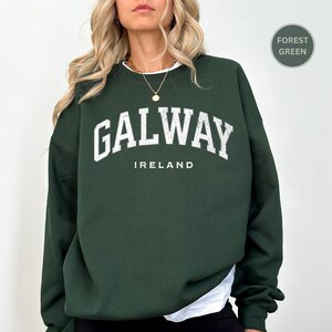 Woman wears forest green sweatshirt with Galway, Ireland in a marine vintage style text. Option to customise.