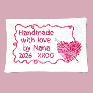 May include: Embroidered white fabric patch with pink text and a pink yarn heart. The text reads "Handmade with love by Nana 2026 XXOO". A crochet hook is inserted into the yarn heart.