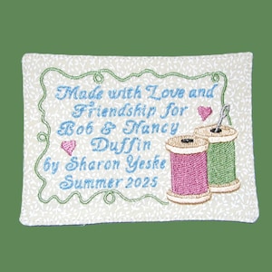 May include: Embroidered patch with the text "Made with Love and Friendship for Bob & Nancy Duffin by Sharon Yeske Summer 2025." Features a green floral border, two spools of thread, and pink hearts.