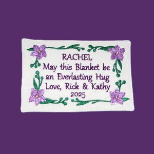 May include: White embroidered fabric with purple flowers and green leaves. The text reads "Rachel, May this Blanket be an Everlasting Hug, Love, Rick & Kathy, 2025".