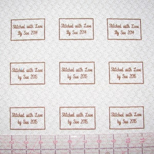 May include: Nine brown rectangular fabric labels with white embroidery. The labels read "Stitched with Love" followed by "By Sue 2014" or "by Sue 2015".