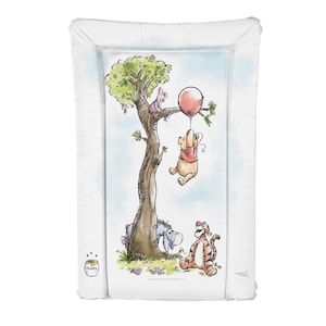 May include: A Winnie the Pooh changing mat with a white background and a colourful illustration of Winnie the Pooh, Piglet, Eeyore, and Tigger. The illustration shows Winnie the Pooh holding a red balloon, Piglet is in a tree, Eeyore is looking up at Winnie the Pooh, and Tigger is walking towards the right side of the mat. The mat has a white border and the words "Honey" and "Cotswold Collection" are printed on the mat.