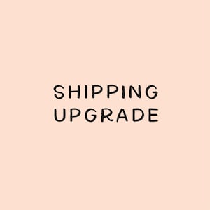 May include: A square graphic with a solid light peach background featuring the text SHIPPING UPGRADE written in simple, black, sans-serif capital letters centered in the middle of the image. The text is clear and easy to read against the background.