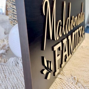 May include: A black wooden sign with the words "Maldonado Family" in gold lettering. A small leaf design is below the text.