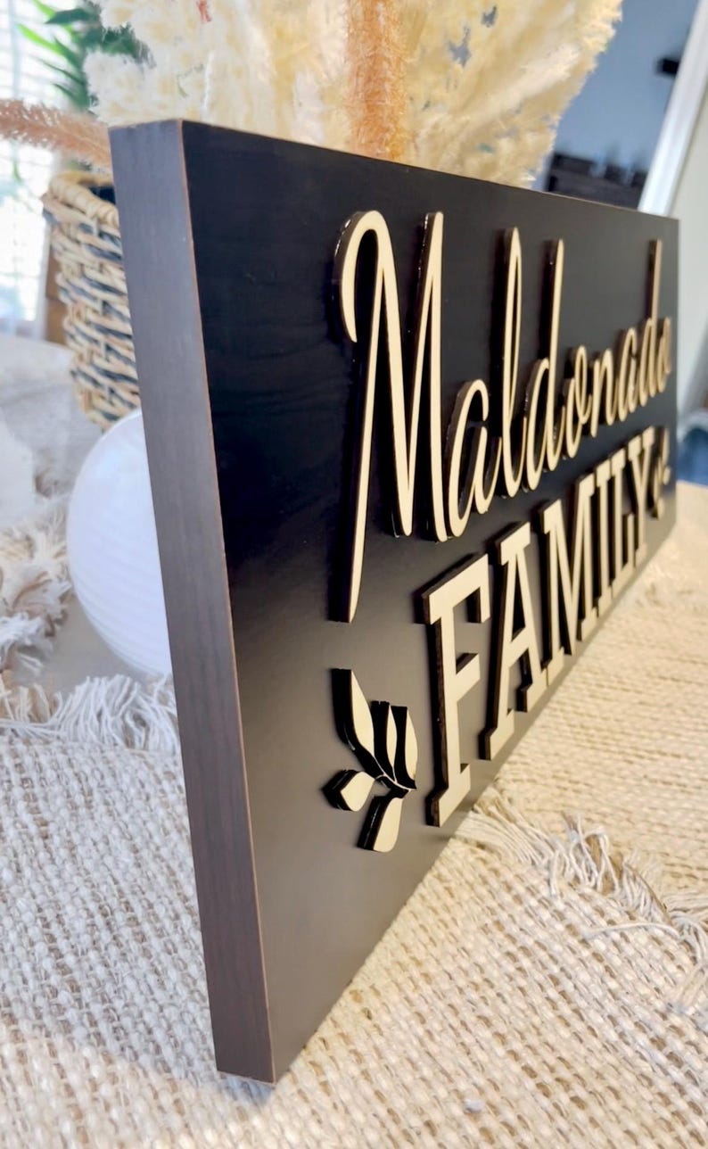 May include: A black wooden sign with the words "Maldonado Family" in gold lettering. A small leaf design is below the text.