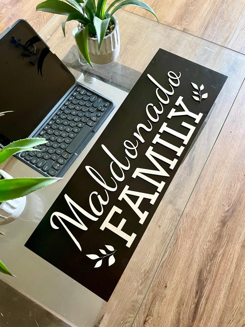 May include: Black wooden sign with white lettering that reads "Maldonado Family" with a leafy design on either side of the text.