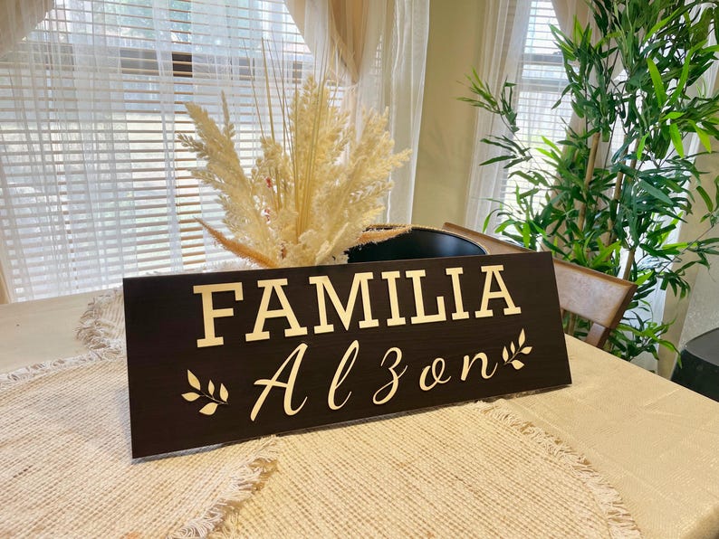 May include: A dark brown wooden sign with the words "FAMILIA Alzon" in gold lettering and a small gold leaf design on each side of the text.