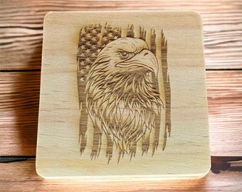 Puede incluir: Placa cuadrada de madera con un diseño grabado con láser. El diseño presenta una bandera estadounidense con la cabeza de un águila en el centro. El águila mira hacia la derecha y las rayas y estrellas de la bandera son visibles.
