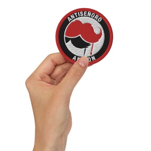 May include: A red, white, and black embroidered patch with the text "Anti-Senoro" and a red mustache with a black drip.