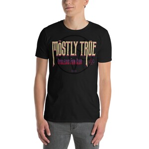 以下が含まれることがあります： 「MOSTLY TRUE」の文字がヴィンテージ風にデザインされた黒いTシャツ。「DYSLEXIC FAN CLUB」の文字がその下に配置されています。テキストの後ろには五芒星のデザインがあります。Tシャツは人が着用しています。