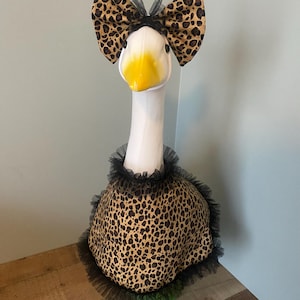 May include: A decorative goose figurine with a white head and neck, a yellow beak, and a leopard print bow and body. The body is trimmed with black tulle, creating a whimsical and stylish look.
